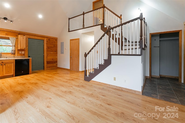 kitchen featuring black dishwasher, high vaulted ceiling, light hardwood / wood-style floors, and wood walls