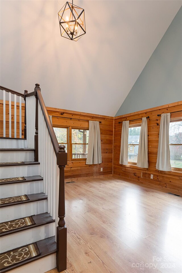 staircase with a notable chandelier, hardwood / wood-style flooring, high vaulted ceiling, and wooden walls