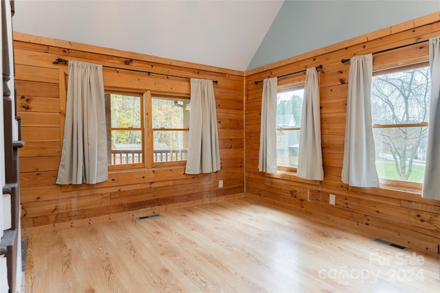 spare room featuring light hardwood / wood-style floors, lofted ceiling, and wooden walls