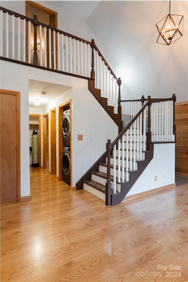 stairway with an inviting chandelier, stacked washer / dryer, hardwood / wood-style flooring, and high vaulted ceiling