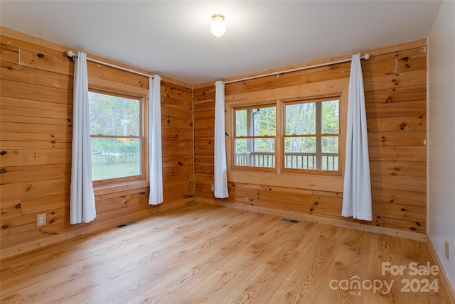 empty room featuring wooden walls, light wood-type flooring, and a wealth of natural light