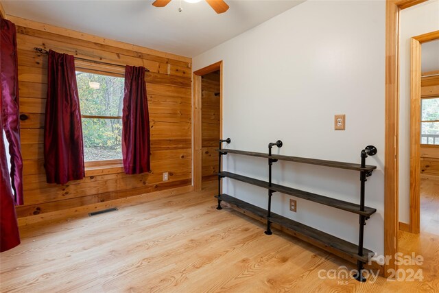 bedroom featuring wooden walls, multiple windows, light wood-type flooring, and ceiling fan