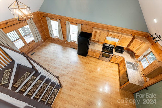 interior space featuring light brown cabinets, light hardwood / wood-style floors, pendant lighting, wooden walls, and a chandelier