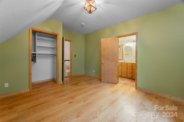 unfurnished bedroom featuring a closet, light hardwood / wood-style flooring, sink, vaulted ceiling, and ensuite bathroom