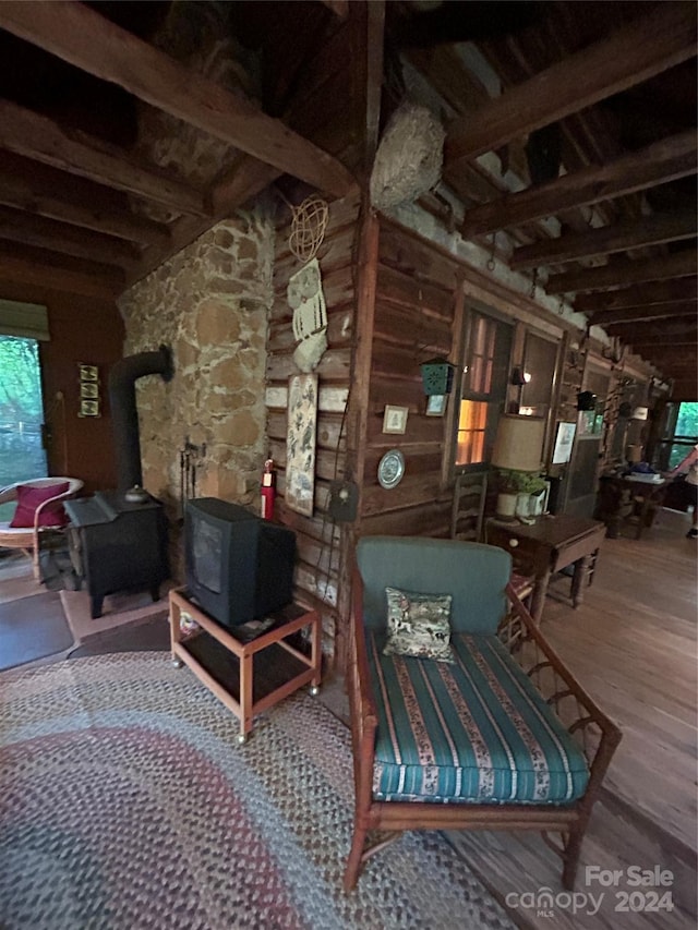 sitting room featuring beam ceiling, wooden walls, hardwood / wood-style flooring, and a wood stove