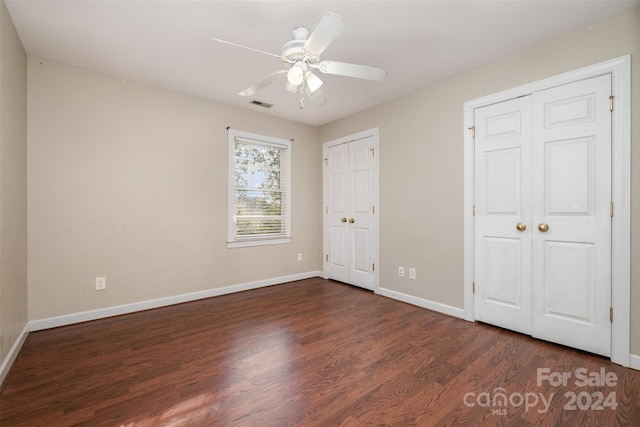 unfurnished bedroom featuring ceiling fan, dark hardwood / wood-style flooring, and two closets