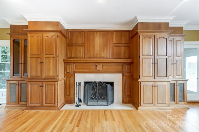 unfurnished living room with a tiled fireplace, crown molding, and light wood-type flooring