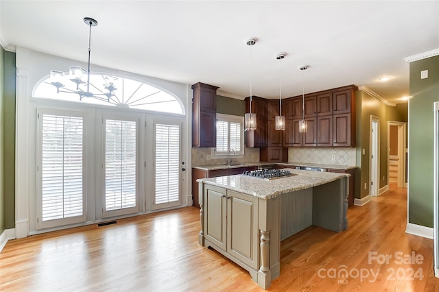 kitchen with light stone countertops, light wood-type flooring, tasteful backsplash, decorative light fixtures, and a kitchen island