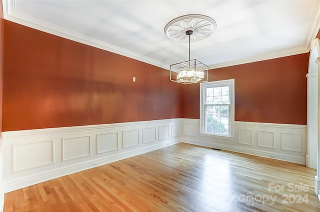 spare room with an inviting chandelier, light hardwood / wood-style floors, and ornamental molding