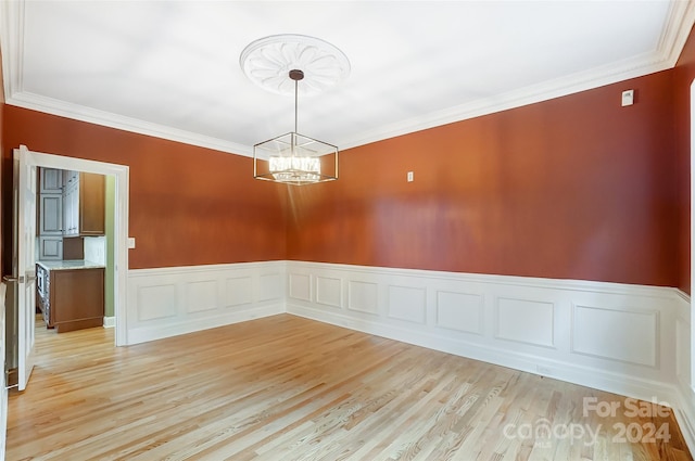 empty room with crown molding, light hardwood / wood-style floors, and a notable chandelier