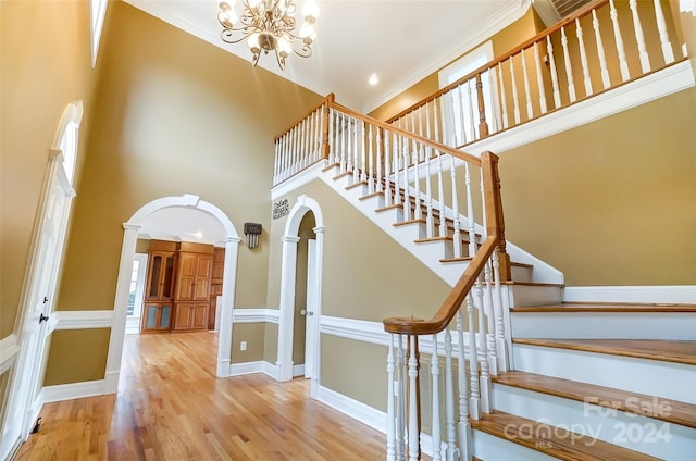 stairway featuring crown molding, hardwood / wood-style floors, a towering ceiling, and an inviting chandelier