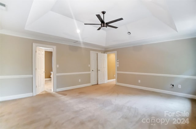 carpeted empty room with a raised ceiling, ceiling fan, and ornamental molding