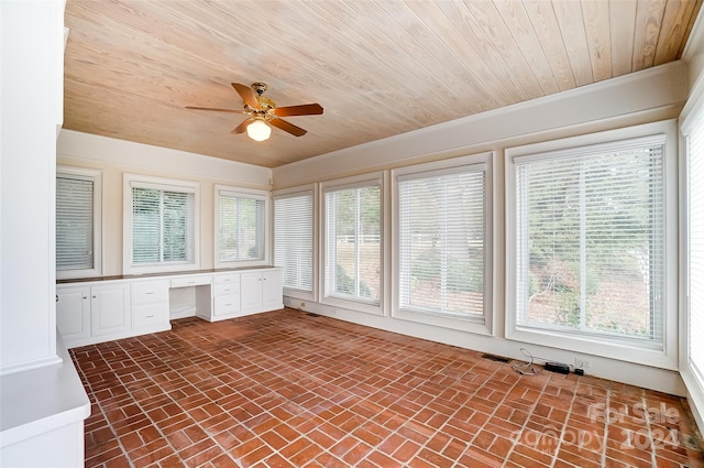 unfurnished sunroom featuring ceiling fan, built in desk, and wood ceiling