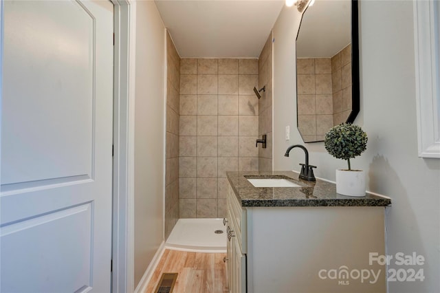 bathroom with a tile shower, vanity, and wood-type flooring