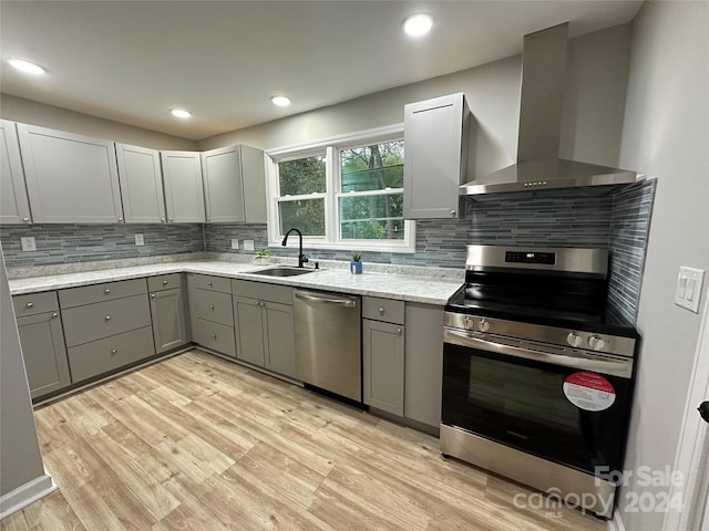 kitchen with decorative backsplash, appliances with stainless steel finishes, light wood-type flooring, sink, and wall chimney range hood