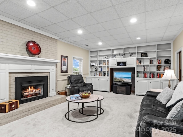 living room featuring built in shelves, light carpet, a fireplace, and a paneled ceiling