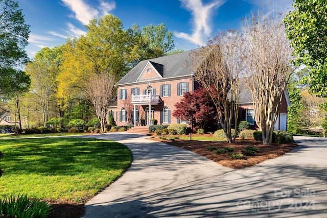 colonial home with a garage, a balcony, and a front lawn