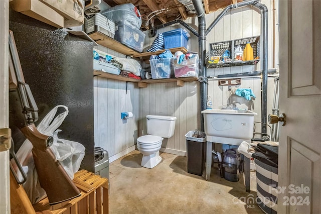 bathroom with toilet, wooden walls, and concrete flooring