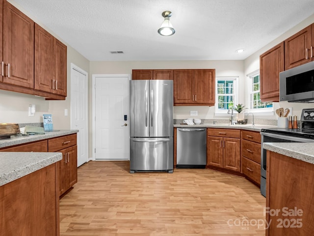 kitchen featuring light stone counters, stainless steel appliances, a textured ceiling, and light wood-type flooring