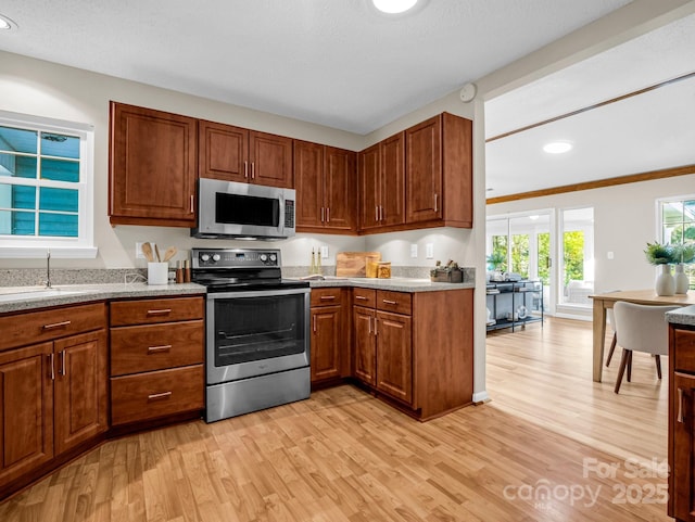 kitchen with appliances with stainless steel finishes, sink, light hardwood / wood-style floors, light stone countertops, and a textured ceiling