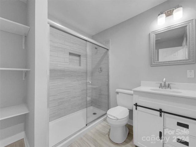 bathroom with vanity, toilet, hardwood / wood-style flooring, and a shower with door