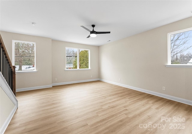 empty room with light wood-style flooring, stairs, baseboards, and a wealth of natural light