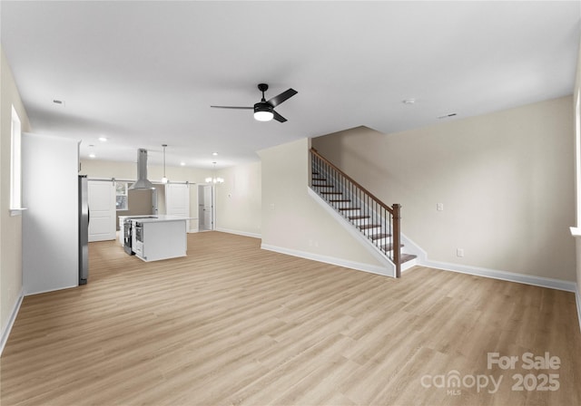 unfurnished living room with baseboards, stairs, ceiling fan with notable chandelier, light wood-style floors, and recessed lighting