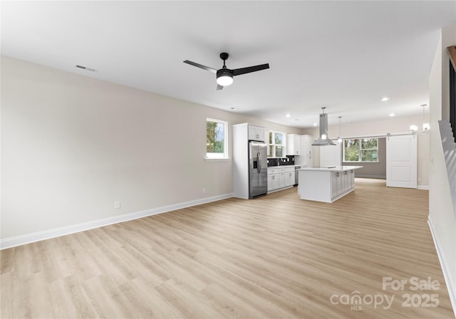 unfurnished living room with a wealth of natural light, a barn door, light wood-style flooring, and a ceiling fan