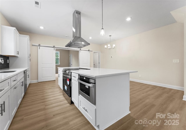 kitchen with a barn door, island exhaust hood, white cabinetry, and light countertops