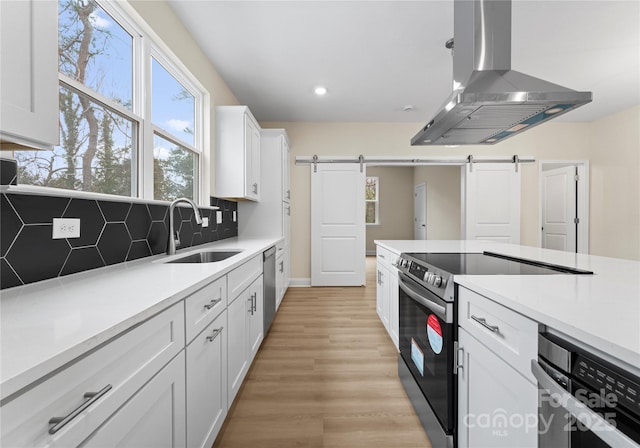 kitchen with stainless steel appliances, light countertops, a barn door, white cabinets, and island range hood