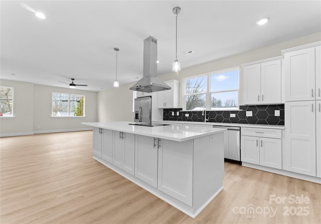 kitchen featuring island range hood, stainless steel appliances, a kitchen island, white cabinets, and decorative light fixtures