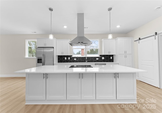 kitchen featuring island exhaust hood, a large island, a barn door, white cabinets, and stainless steel fridge