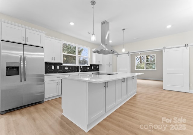 kitchen with a barn door, island exhaust hood, light countertops, white cabinetry, and stainless steel refrigerator with ice dispenser