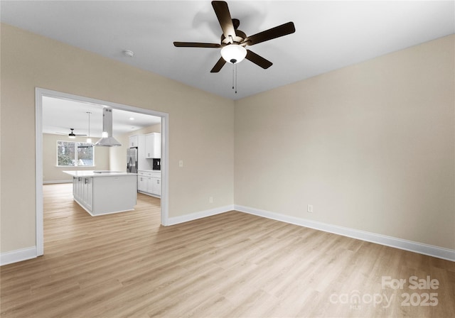 unfurnished room featuring baseboards, a ceiling fan, and light wood-style floors