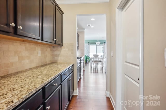 kitchen with dark brown cabinetry, dark wood-type flooring, light stone counters, backsplash, and crown molding