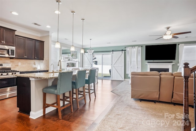 kitchen featuring pendant lighting, a kitchen bar, a kitchen island with sink, dark brown cabinets, and appliances with stainless steel finishes