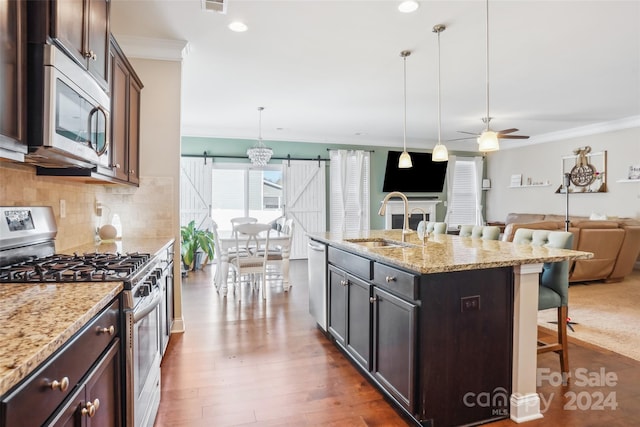 kitchen with stainless steel appliances, a kitchen island with sink, sink, a barn door, and a breakfast bar area