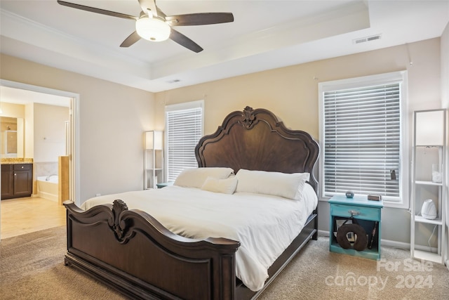 carpeted bedroom featuring a tray ceiling, ensuite bath, and ceiling fan