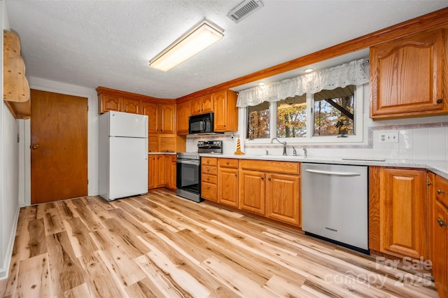 kitchen featuring visible vents, light countertops, appliances with stainless steel finishes, light wood-type flooring, and brown cabinetry