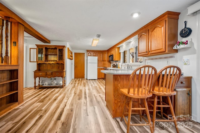 kitchen featuring brown cabinetry, freestanding refrigerator, light wood-style floors, and a peninsula