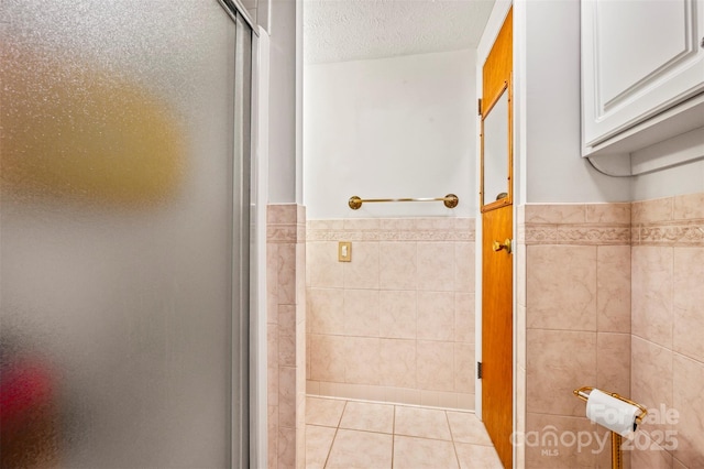 bathroom with a wainscoted wall, tile walls, a stall shower, a textured ceiling, and tile patterned flooring