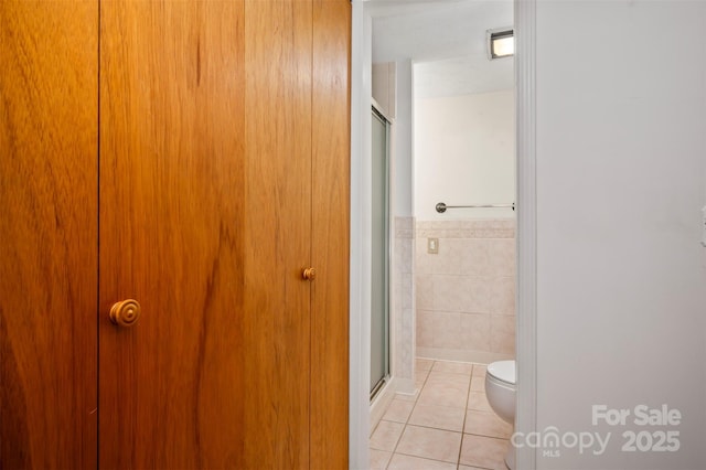 bathroom featuring toilet, a shower stall, tile walls, and tile patterned floors