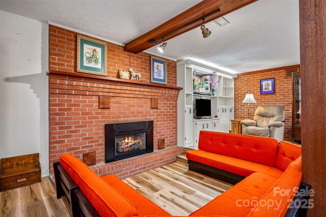 living area with beam ceiling, a fireplace, a textured ceiling, and wood finished floors