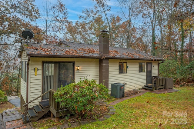 back of house with entry steps, a lawn, a chimney, and central AC unit