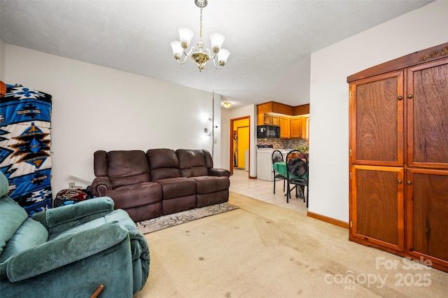 living area featuring a chandelier, light tile patterned floors, light colored carpet, baseboards, and washer and dryer