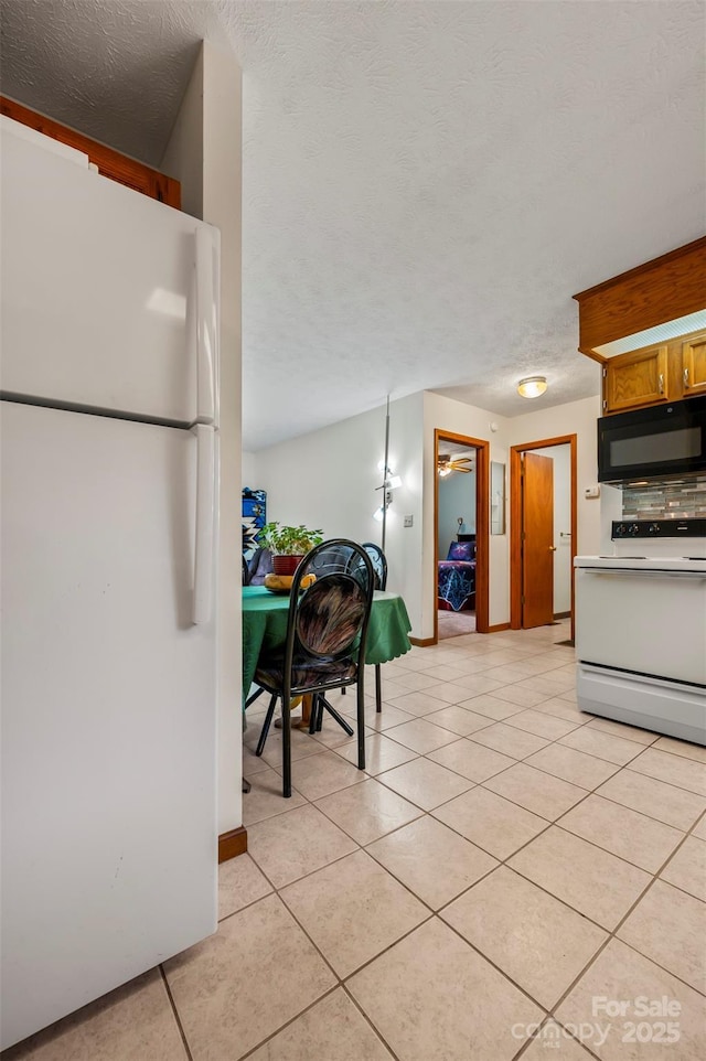 kitchen with a textured ceiling, white appliances, and light tile patterned flooring