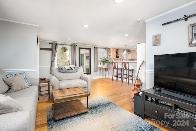 living room featuring light hardwood / wood-style floors, ornamental molding, and a barn door