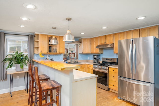 kitchen with appliances with stainless steel finishes, kitchen peninsula, decorative light fixtures, and light hardwood / wood-style floors