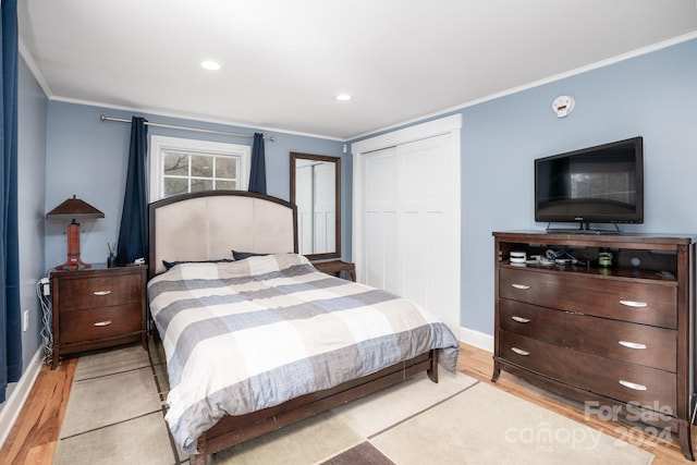 bedroom with light hardwood / wood-style floors, crown molding, and a closet