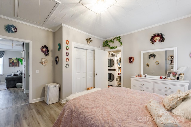 bedroom with a closet, crown molding, light wood-type flooring, and stacked washing maching and dryer